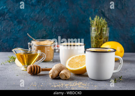 Zwei emaillierten Becher mit Zitrone Tee, Ingwer, Thymian, Zimt, Anis und Honig auf grauem Hintergrund Stockfoto