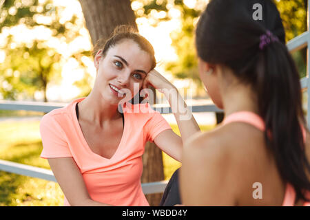 Bild von attraktiven fitness Frauen in Sportswear lächelnd und zusammen reden während der Sitzung in Green Park Stockfoto