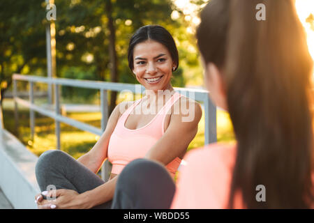 Bild von Happy fitness Frauen in Sportswear lächelnd und zusammen reden während der Sitzung in Green Park Stockfoto