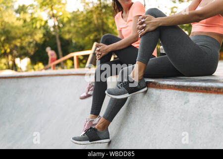 Zugeschnittenes Bild der junge schlanke Frauen in Sportkleidung sitzt und spricht konkrete Sportplatz Stockfoto