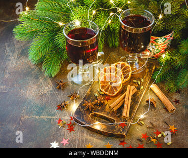 Glas Tassen heißer Glühwein mit Gewürzen und trockenen orange Stücke auf Holz Schneidebrett auf dunklem Hintergrund. Traditionelle weihnachtliche Getränk Stockfoto