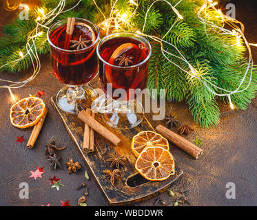 Glas Tassen heißer Glühwein mit Gewürzen und trockenen orange Stücke auf Holz Schneidebrett auf dunklem Hintergrund. Traditionelle weihnachtliche Getränk Stockfoto