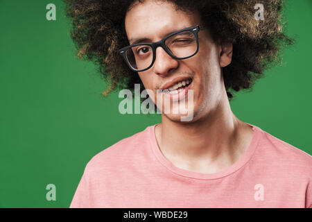 Bild einer jungen curly Kerl über grüne Wand Hintergrund Sie zwinkern isoliert posieren. Stockfoto