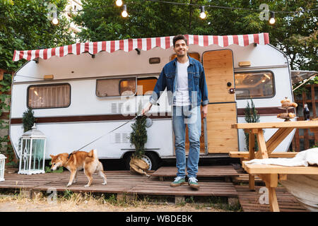 Portrait von Glücklich lächelnde Mann denim Kleidung wandern mit Roter Hund in der Nähe von Haus auf Rädern im Freien Stockfoto