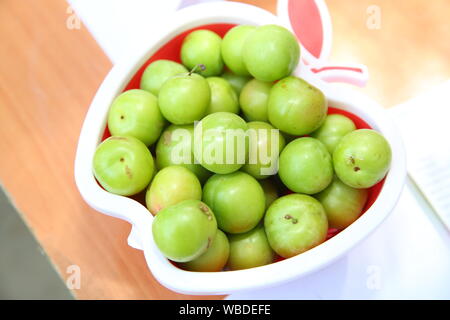 Grüne saure Pflaumen im Apple Platte, Pflaume Bilder auf die weiße Masse, Qualität und natürlichen Leben spendende Grüne saure Pflaumen. Grüne saure Pflaumen in der Pla Stockfoto