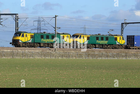 Zwei Klasse 90 elektrische Lokomotiven, schleppen Sie einen Behälter mit einem Güterzug entlang der West Coast Main Line, Staffordshire, England, im Jahr 2018. Stockfoto