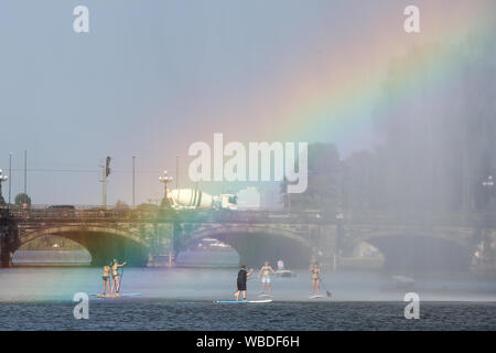 Hamburg, Deutschland. 26 Aug, 2019. Auf Stand-up-Boards, kühlen Sie sich bei Temperaturen über 30 Grad Celsius an der Binnenalster Fontäne auf der Binnenalster, wo Sonnenlicht bricht und die Farben des Regenbogens zeigen. Credit: Bodo Marks/dpa/Alamy leben Nachrichten Stockfoto