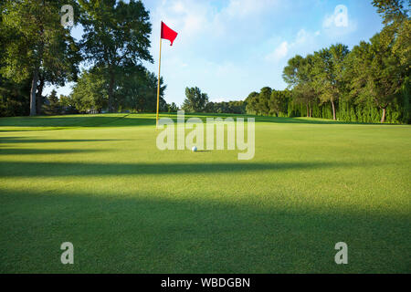 Low Angle View eines Golf Grün mit roten Flagge und die Kugel an einem sonnigen Nachmittag Stockfoto