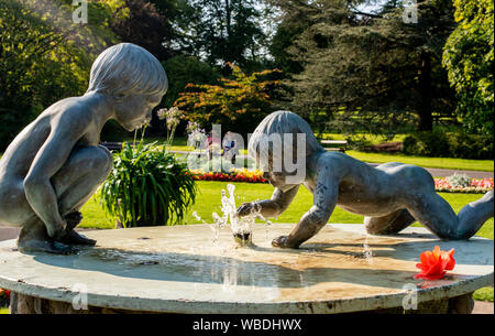 Statuen der Kinder am Brunnen, Frauen ruht auf einer Parkbank im Hintergrund bei sehr heißem Wetter, Bank Holiday Montag, Valley Gardens, Harrogate, UK, 26. August 2019 Stockfoto