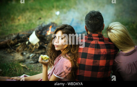 Eine Gruppe von Freunden mit Picknick im Sommer. Brunette Mädchen essen Green Apple während lehnte sich auf ihre Freundin. Vitamine, Gesundheit und Wohlbefinden. Stockfoto