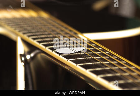 White Pick unter zwischen Strings und Bund auf dem Griffbrett der Gitarre stecken Stockfoto