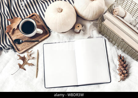 Herbst das Frühstück im Bett Komposition. Leere Notepad öffnen, Tagebuch mockup. Tasse Kaffee, weißen Kürbisse, Plaid, Eichenlaub und alte Bücher. Bettwäsche backgroun Stockfoto