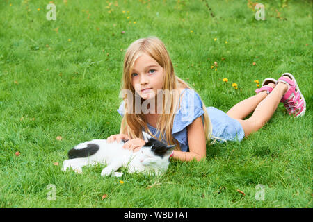 Kind blonde Mädchen spielen und streicheln mit Katze auf Gras Im Sommer Stockfoto