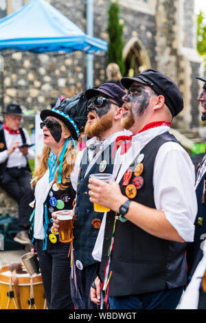 Sandwich Folk und Ale Festival event, UK. Traditionelle englische Volkstänzer, Dead Horse morris Seite, mit geschwärzten Gesichtern, in der Straße stehend, Gesang. Stockfoto