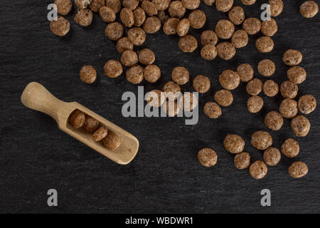 Menge ganze Schokolade Kugel Frühstücksflocken mit Holz- schaufel flatlay am grauen Stein Stockfoto