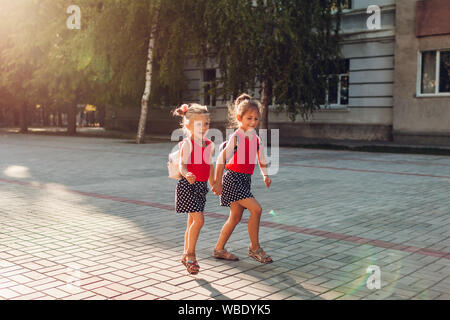 Glückliche Schwestern Mädchen, Rucksäcke und laufen. Kinder Schüler Spaß in der Nähe der Schule. Bildung. Zurück zur Schule Stockfoto