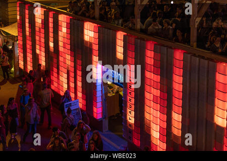 Stadtfest Brugg 24. august 2019. Nacht der Fotografie. Rot beleuchtete Wand von Kubus Kolor mit Menschen auf der Oberseite und den Menschen zu Fuß Stockfoto