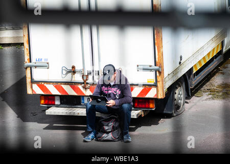 Mann mit Laptop sitzen auf der Rückseite eines verlassenen Lieferwagen in privaten Parkplatz versucht, einen kostenlosen WLAN-Signal von der in der Nähe von Gebäude zu fangen. Stockfoto