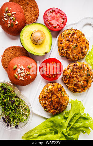 Zutaten für vegane Burger auf einem weißen Hintergrund. Bohnen Burger, Rosa rote Beete Brötchen, Sämlinge, Avocados und Gemüse. Stockfoto