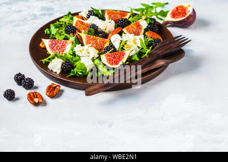 Salat mit Feigen, Fetakäse und Brombeeren in eine hölzerne Platte auf einem weißen Hintergrund. Stockfoto