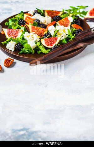 Salat mit Feigen, Fetakäse und Brombeeren in eine hölzerne Platte auf einem weißen Hintergrund. Stockfoto