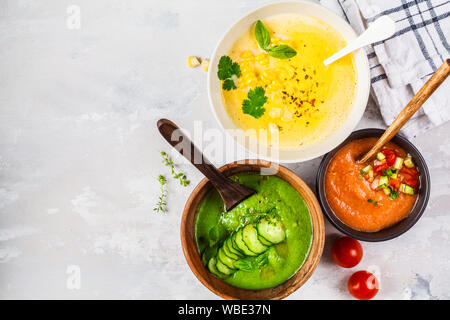 Drei verschiedene pflanzliche Creme Suppen in Schalen auf grauem Hintergrund. Mais, Gurke und Gazpacho Suppen. Stockfoto