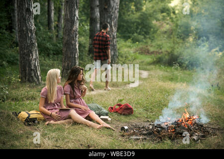 Junge Mädchen das Lesen von Büchern in Wald oder Park. Schöne Frauen sitzen am Lagerfeuer. Kerl zu Fuß auf dem Weg in den Wald Stockfoto