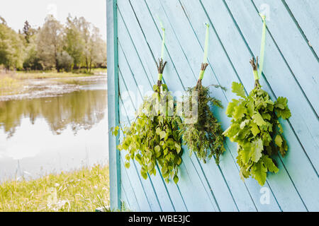 Eiche, Birke, Wacholder und Eiche Sauna bringt Besen aufhängen und trocknen auf sauna Haus Wand mit wunderschönen, natürlichen See. Traditionelle finnische Sauna Stockfoto