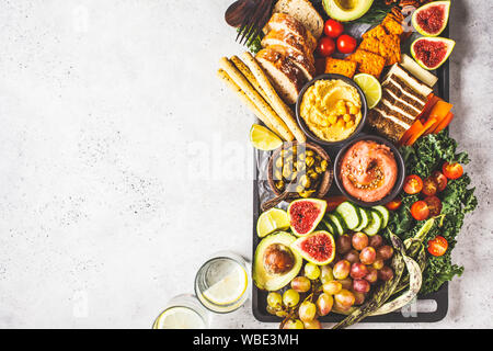 Vegane Vorspeise Platter. Hummus, Tofu, Gemüse, Obst und Brot auf einem schwarzen, weißen Hintergrund. Stockfoto