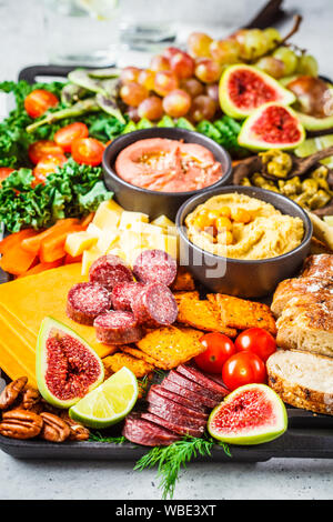 Fleisch und Käse Vorspeise Platter. Wurst, Käse, Hummus, Gemüse, Obst und Brot auf einem schwarzen, weißen Hintergrund. Stockfoto