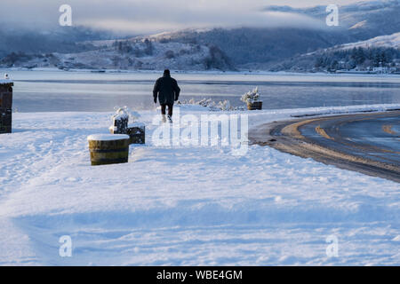 Solo Männer gehen auf Schnee lochside Pfad in Lochcarron, Wester Ross, NW Highlands von Schottland Stockfoto