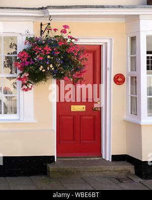 Frisch cremefarbenen Haus/Haus mit roten Haustür gemalt, weiße Schiebefenster und hängenden Korb, Uppingham, England, UK. Stockfoto