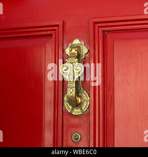 Reich verzierte, dekorative Messing Türklopfer auf rot lackierten Holz- Tür mit Spion Glas Viewer, Großbritannien Stockfoto