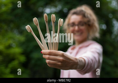 Junge schöne Frau mit blond gelocktem Haar in Rosa hipster Jacke und Brille Holding fünf Bambus Zahnbürsten in die Hand. Null Abfall Konzept Stockfoto