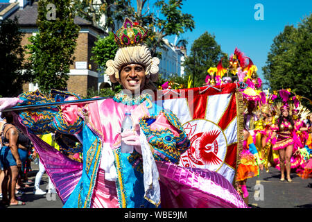 26. August 2019 - Mann, gekleidet in einen Zeitraum Kostüm mit Pulver Perücke, Krone und Flagge in Notting Hill Karneval an einem heißen Feiertag Montag, London, UK Stockfoto