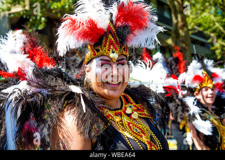 26. August 2019 - Tänzer in eine Feder samba Kopfschmuck lächelnd an Notting Hill Karneval an einem heißen Feiertag Montag, London, UK gekleidet Stockfoto