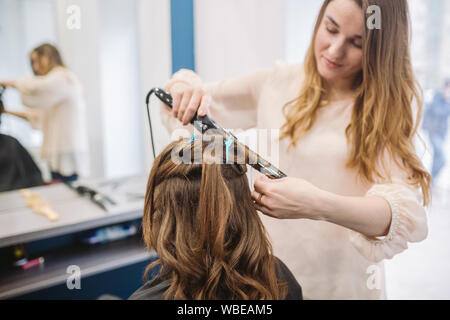 Schönheit, Frisur Konzept, glückliche junge Frau und Friseur mit Haar Eisen, Frisur, Haar Salon. Frau in Haar stilisierte Friseur Stockfoto