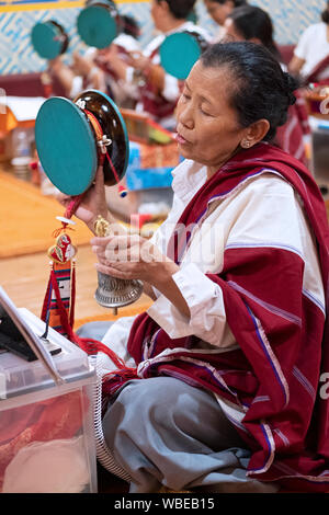 Ein frommer Nepalesischen Buddhistischen betende Frau im Tempel beim Klingeln einer Glocke & Drehen eines Damaru drum. In Elmhurst, Queens, New York City. Stockfoto