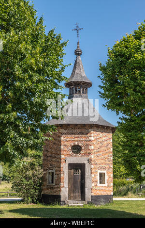 Bokrijk, Belgien - 27. Juni 2019: Red Brick achteckige Kapelle von Metsteren mit dunklen Grau Dach und umgeben von Bäumen. Braune Tür Clos Stockfoto