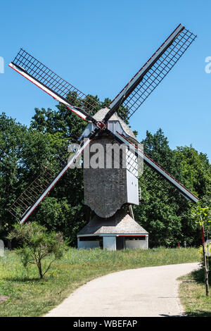 Bokrijk, Belgien - 27. Juni 2019: Mühle von Schulen liegt in der grünen Umgebung von Wiese gesetzt und von Bäumen unter blauem Himmel umgeben. Keine Segel am Flügel. Stockfoto