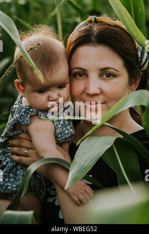 Mutter in ihren Dreißigern mit Tochter posiert im Maisfeld. Warme Sommer Landschaft. Stockfoto