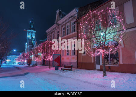 Uschhorod, Ukraine - 06 Jan, 2019: Winter Nacht in der Stadt. wunderbar blau und lila Weihnachtsbeleuchtung. Leere Voloshyna Straße im Schnee bedeckt. Cath Stockfoto