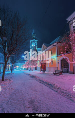 Uschhorod, Ukraine - 06 Jan, 2019: Winter Nacht in der Stadt. wunderbar blau und lila Weihnachtsbeleuchtung. Leere Voloshyna Straße im Schnee bedeckt. Cath Stockfoto
