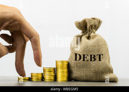 Die nettofinanzschulden Konzept. Ein Mann hand auf Stapel von Münzen und Geld Beutel über Schuld zu zeigen. Stockfoto