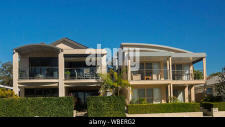 Zwei moderne zweistöckige Häuser mit großen Fenstern, Balkon im Obergeschoss und gepflegten Garten Hecke - unter blauen Himmel bei Tea Gardens, NSW Australien Stockfoto