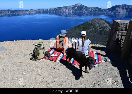 Two young women and their dogs enjoy view of Crater Lake and Wizard Island at Crater Lake National Park, Oregon on a clear summer afternoon. Stockfoto