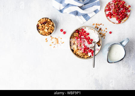 Müsli Schale mit Joghurt und Rote Johannisbeere Beeren auf grauem Beton Hintergrund. Ansicht von oben, kopieren. Sauber Essen, gesundes Frühstück, vegetarisches Essen c Stockfoto