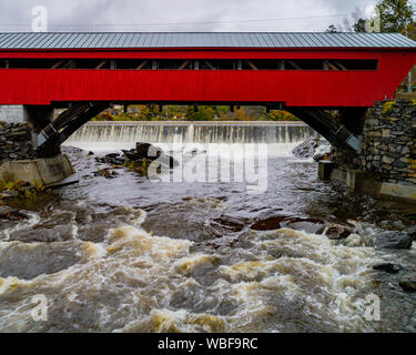 Eine rote Brücke erste 1883 überspannt ein schnell fließender Fluss mit kleinen Wasserkraftwerk Staumauer in Vermont gebaut Stockfoto