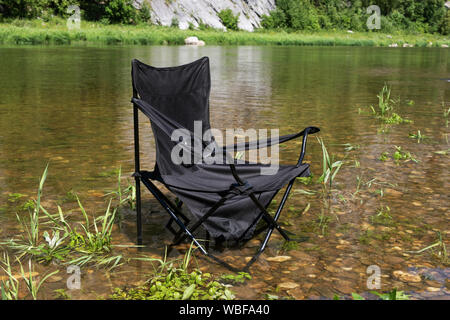 Eine leere Klappstuhl steht im Wasser, niemand in der Nähe ist Stockfoto