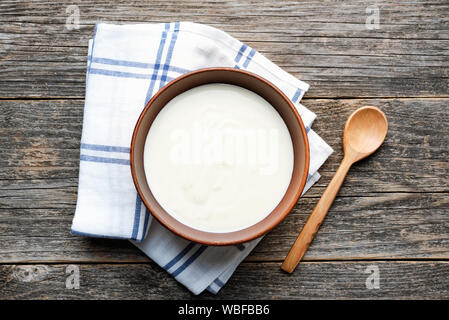 Griechischer Joghurt in eine Schüssel auf Holztisch mit Löffel aus Holz. Ansicht von oben. Gesunde Milchprodukte reich an Kalzium und Eiweiß Stockfoto